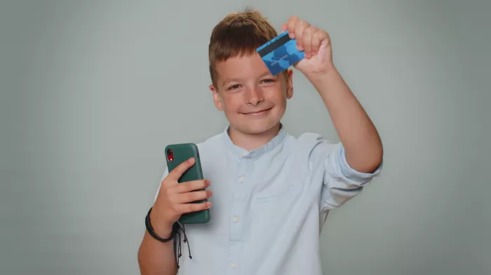 Kisfiú egy bankkártyát és mobiltelefont tart a kezében