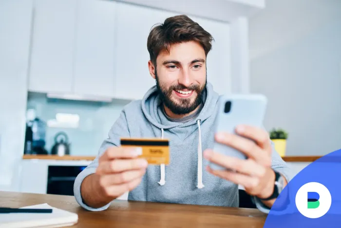 Ingyenes bankkártyát tart a férfi a kezében miközben mobiltelefonon banki értesítő üzenetet olvas