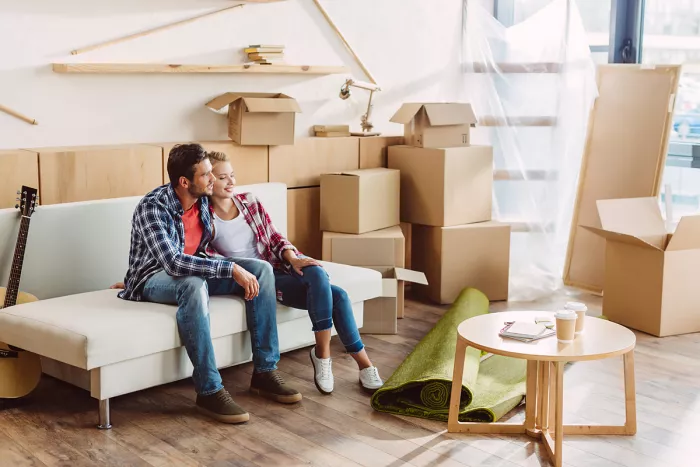 Fiatal pár boldogan ül az új lakásuk nappalijában kibontatlan dobozokkal