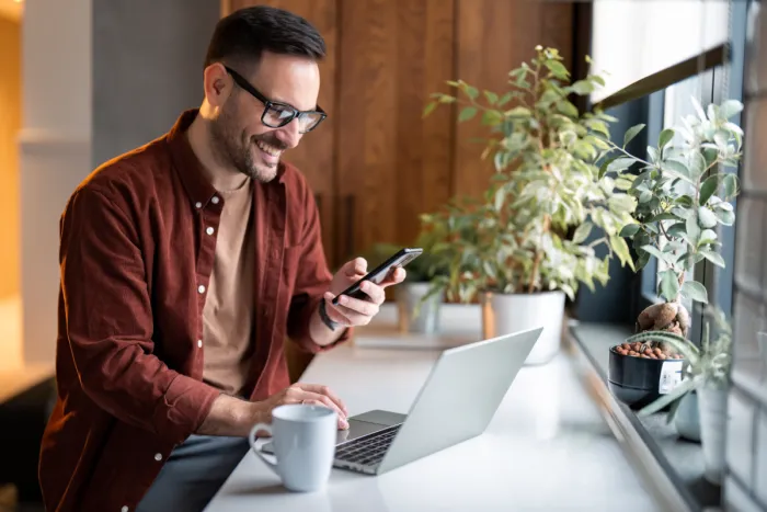 szemüveges férfi laptop előtt telefonnal a kezében