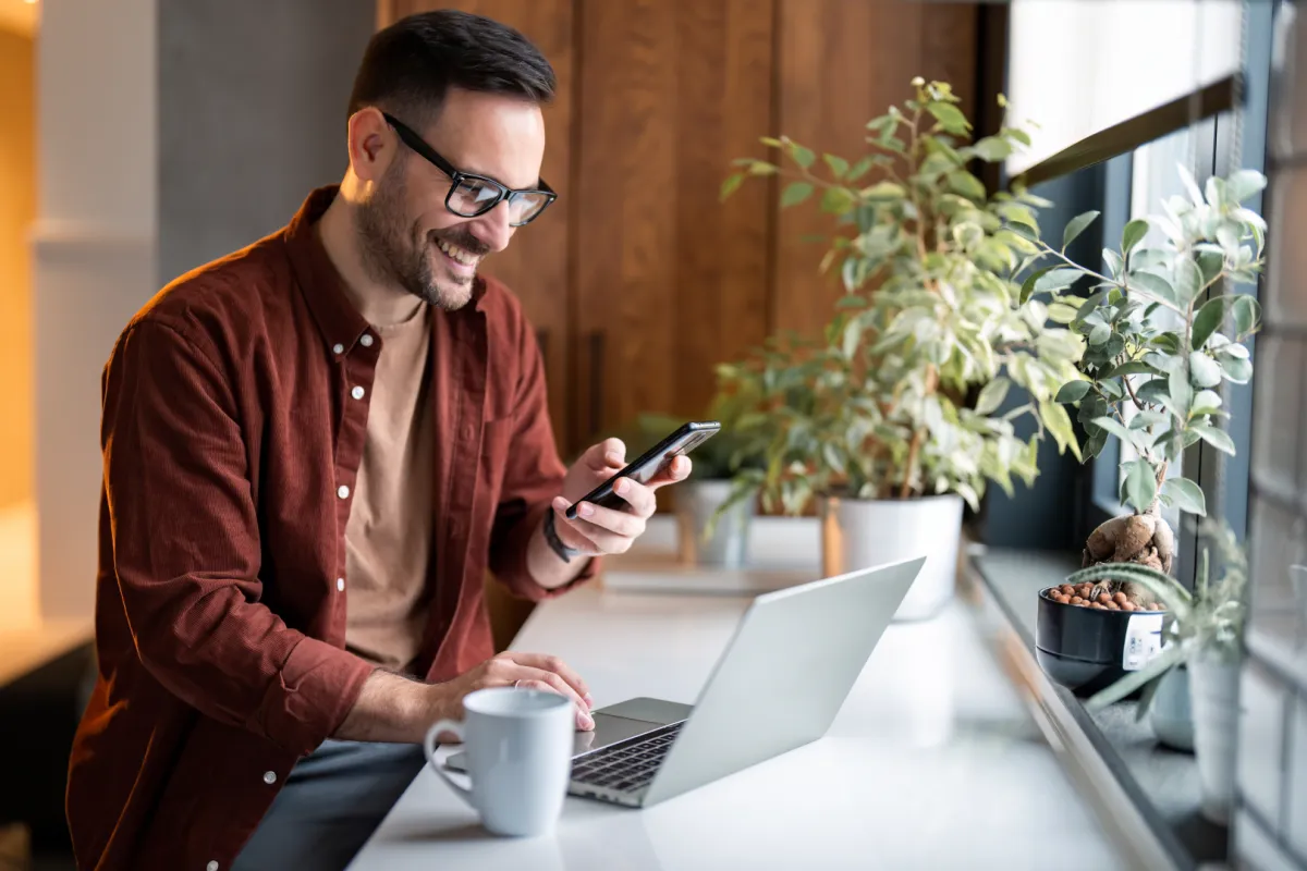 szemüveges férfi laptop előtt telefonnal a kezében