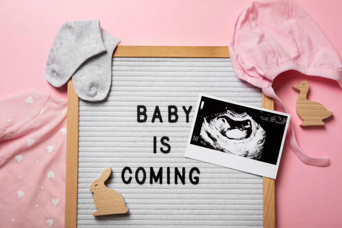 babavárás bejelentése rózsaszínes háttérrel babakelengyével és ultrahangképpel