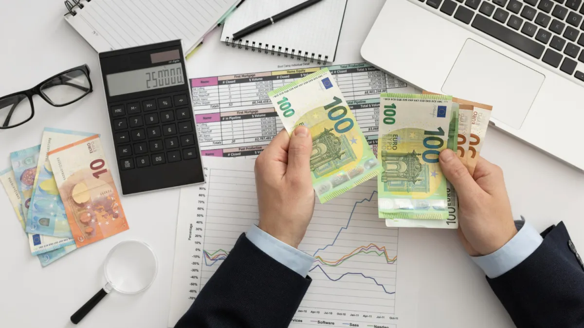 íróasztalon kimutatások számológép laptop és euró bankjegyeket számolgató kéz