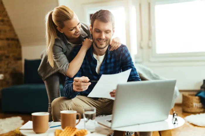 otthoni környezetben laptop előtt dokumentumot néző felszabadult pár
