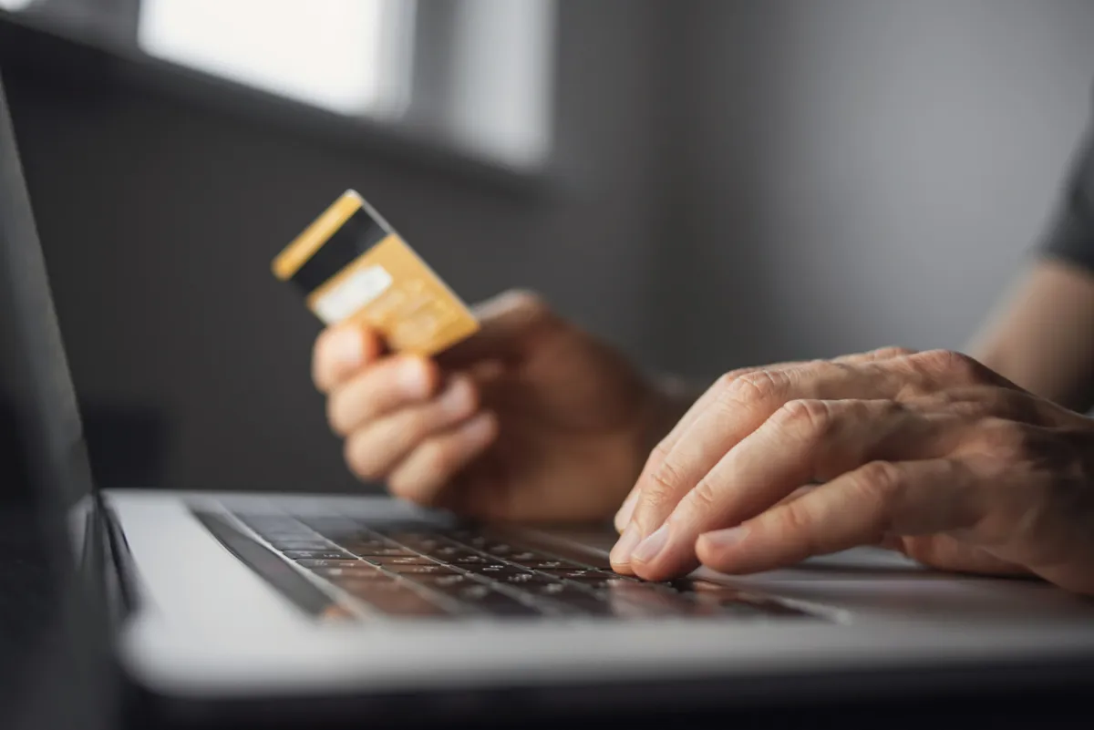 Bankkártyát tart a férfi a kezében miközben a laptopról vásárol