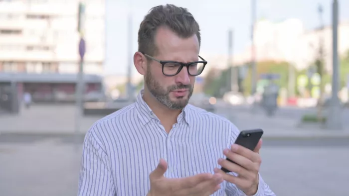 Meglepett férfi olvassa a mobilján, hogy már kamatadót is fizetnie kell a megtakarításai után