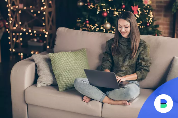 Lány karácsonyi ajándékokat vásárol laptopon a karácsonyfa mellől