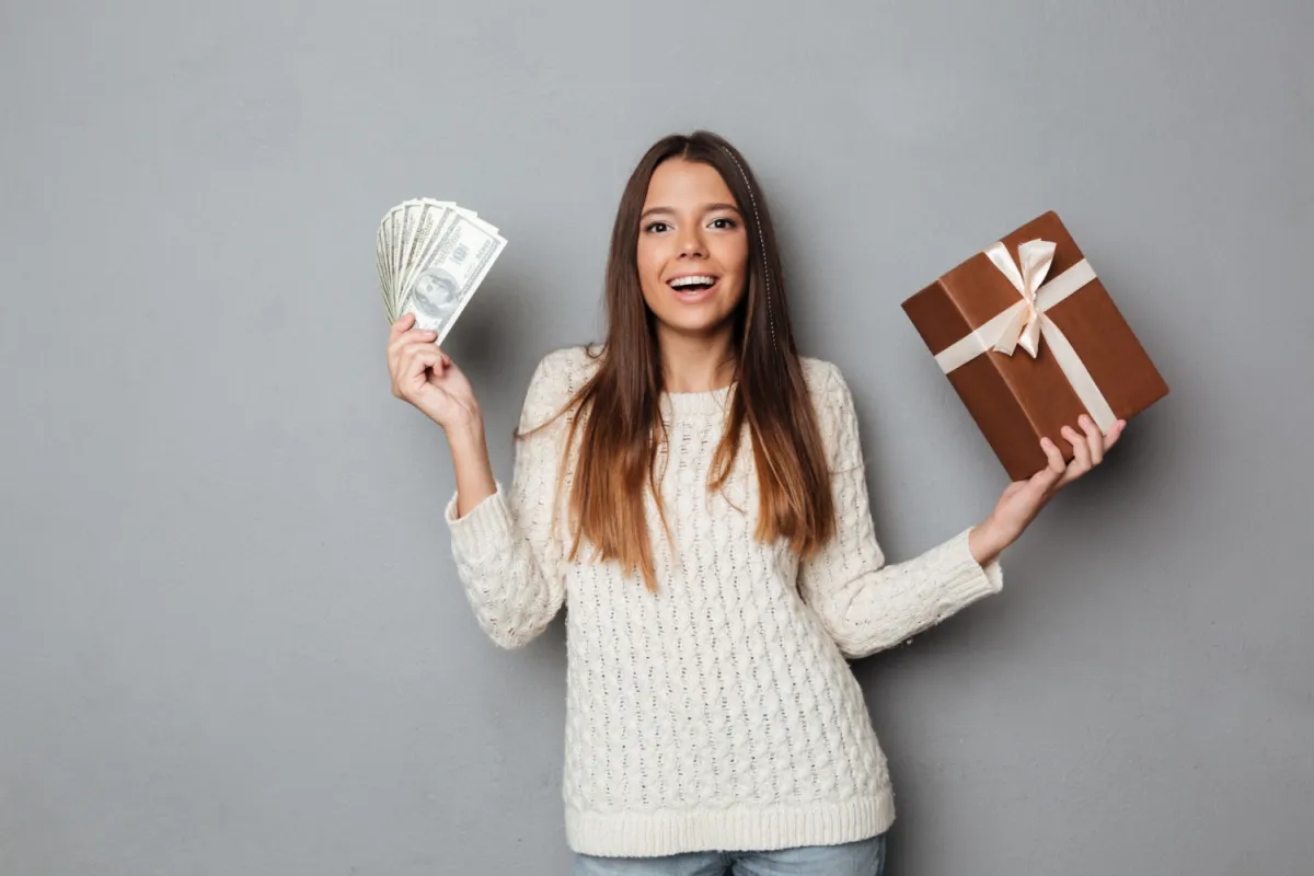 boldog csinos barna lány pénzköteggel és ajándékdobozzal