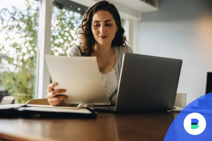 Egy nő szerződést olvas papíron a laptopja mellől