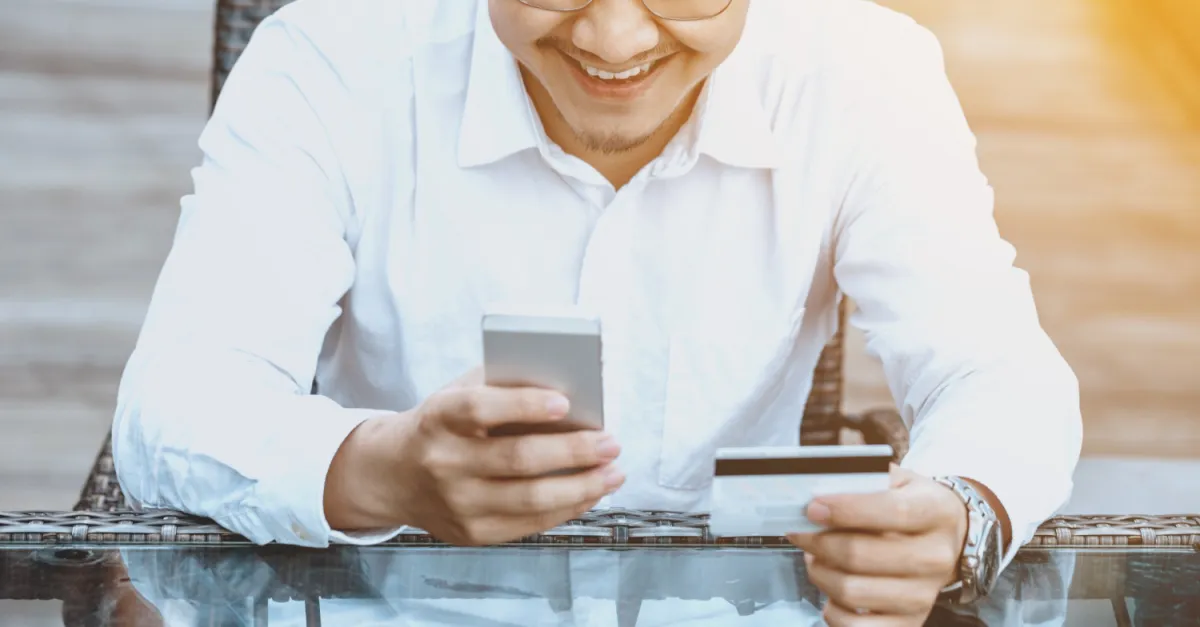 mobiltelefonján a bankkártyájával fizető fiatal férfi