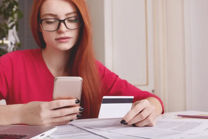 vöröshajú szemüveges csinos lány digitálisan bankol mobillal