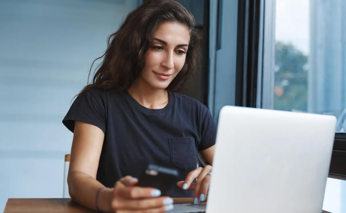 sötétbarna hajú nő laptop előtt mobillal