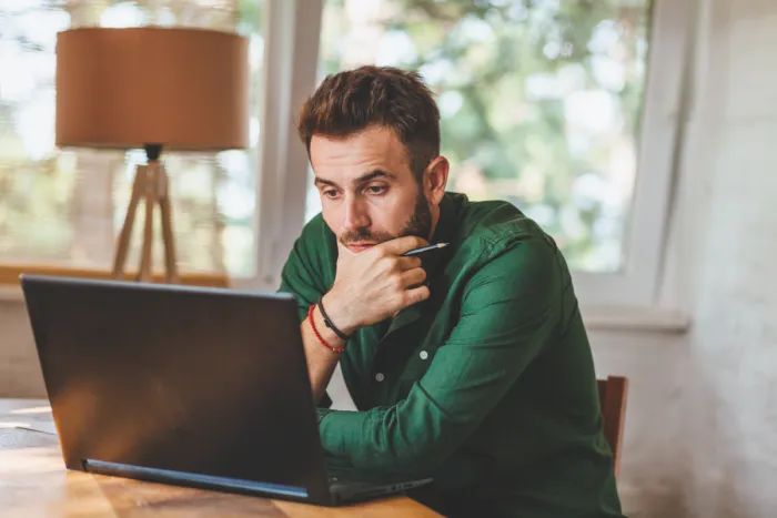 töprengő férfi zöld ingben laptop előtt