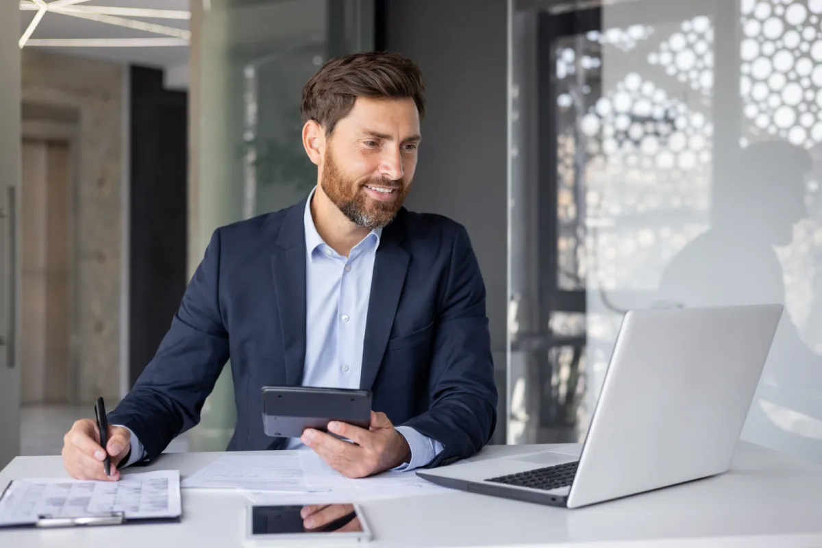 vállalkozó az íróasztalánál laptoppal, mosolyogva ügyeket intéz